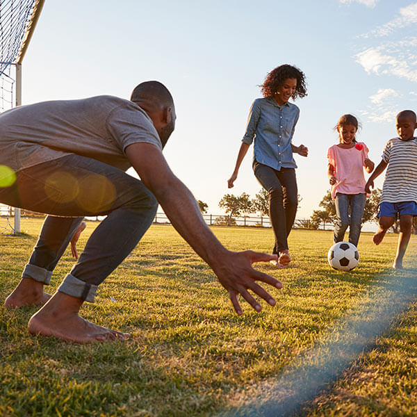 father playing goalie as son kicks soccer ball